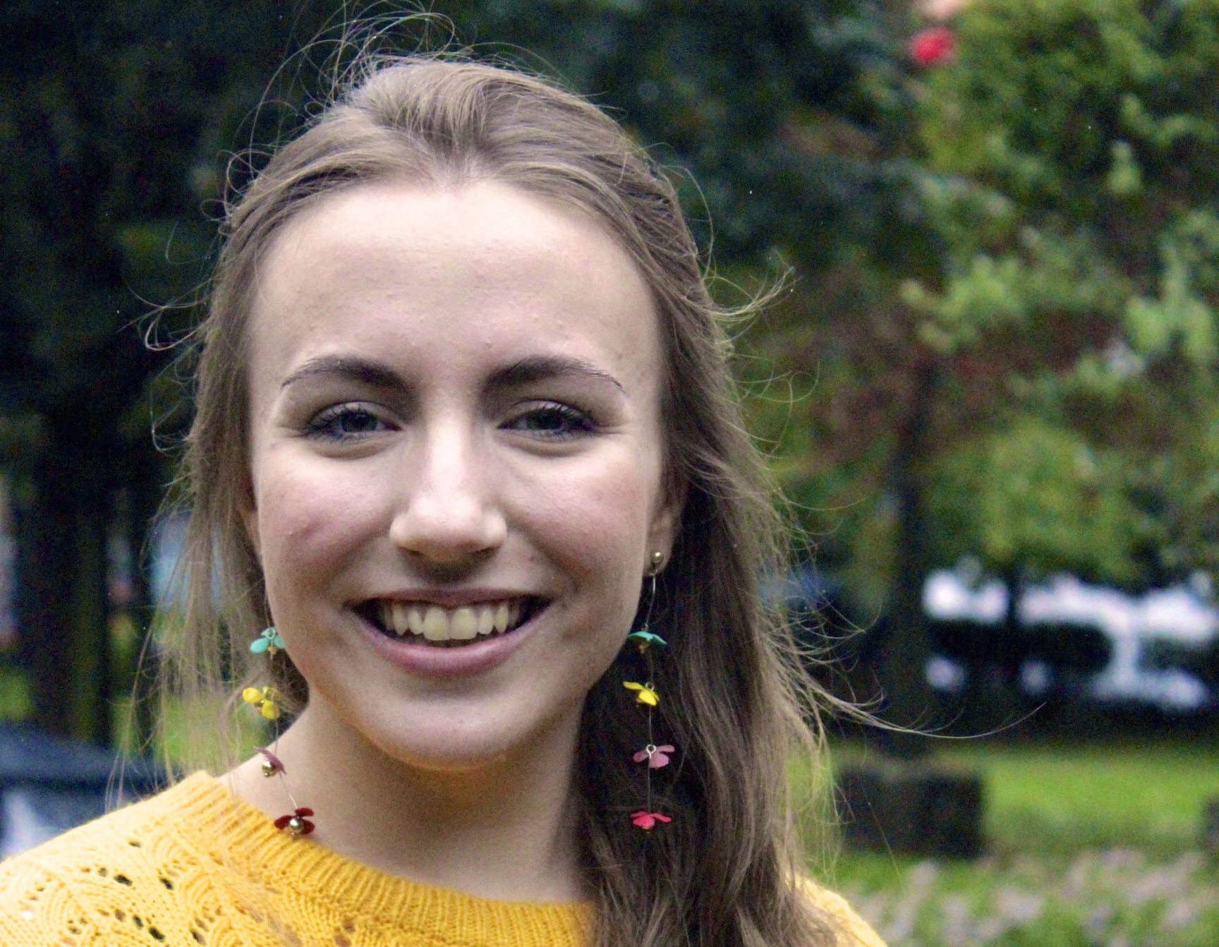 Headshot of Rebecca Anderson, a white woman with long brown hair wearing a yellow knitted jumper and long, dangly earrings with bright flowers on them